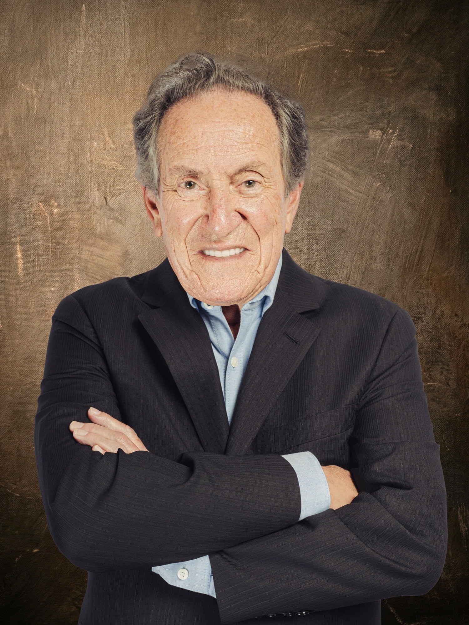 Man with folded arms in a dark blazer against a brown studio backdrop
